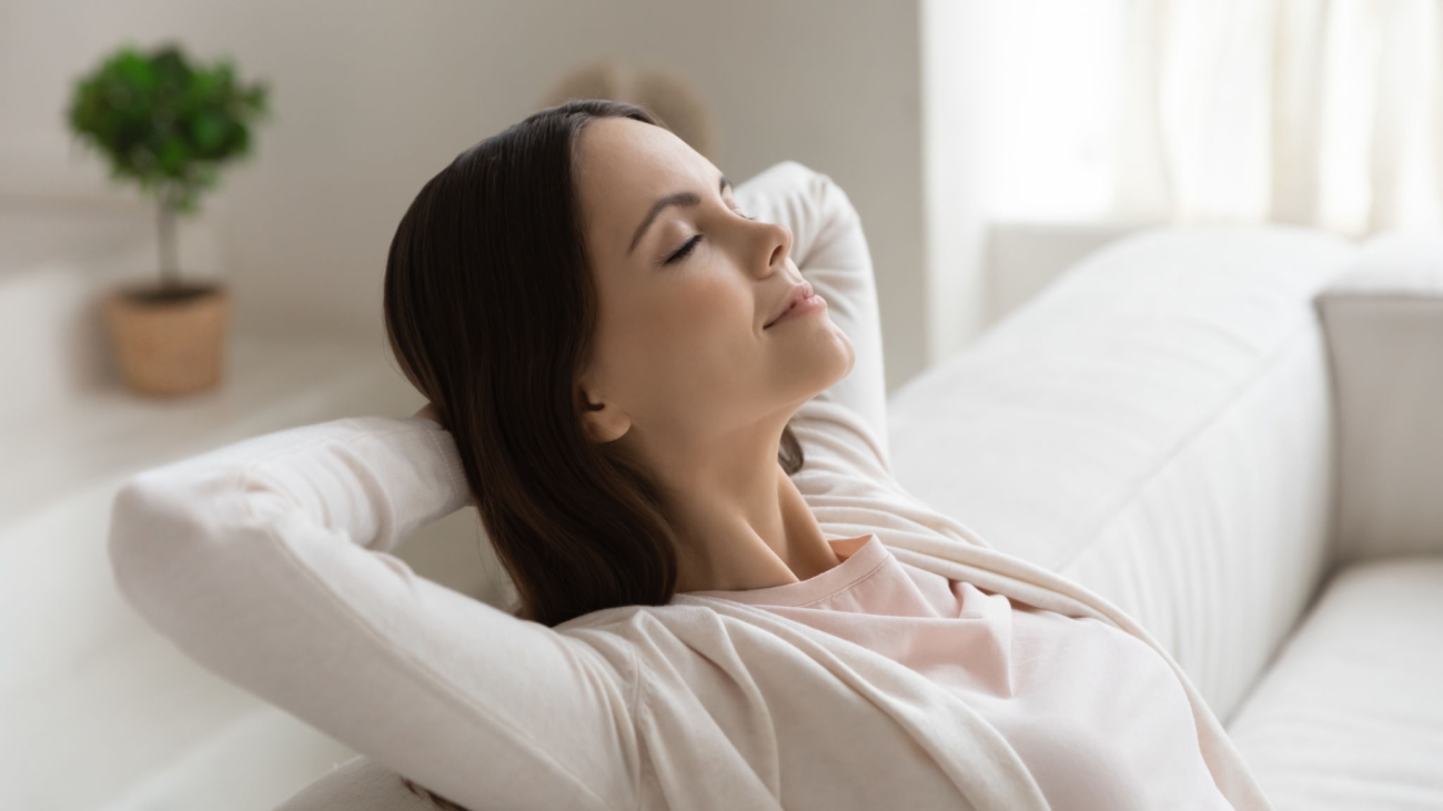 Weekend, at least!.. Tranquil peaceful millennial female enjoying freedom napping dreaming relaxing on couch with closed eyes and hands behind head meditating breathing fresh air feeling happy serene