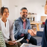 Mature indian man shaking hands with financial advisor at home. Happy smiling couple greeting broker with handshake at home. Multiethnic mid adult man and hispanic woman sealing a contract.