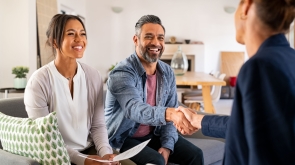 Mature indian man shaking hands with financial advisor at home. Happy smiling couple greeting broker with handshake at home. Multiethnic mid adult man and hispanic woman sealing a contract.