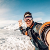 Happy skier taking a selfie on the mountains - Young man having fun skiing downhill in winter forest